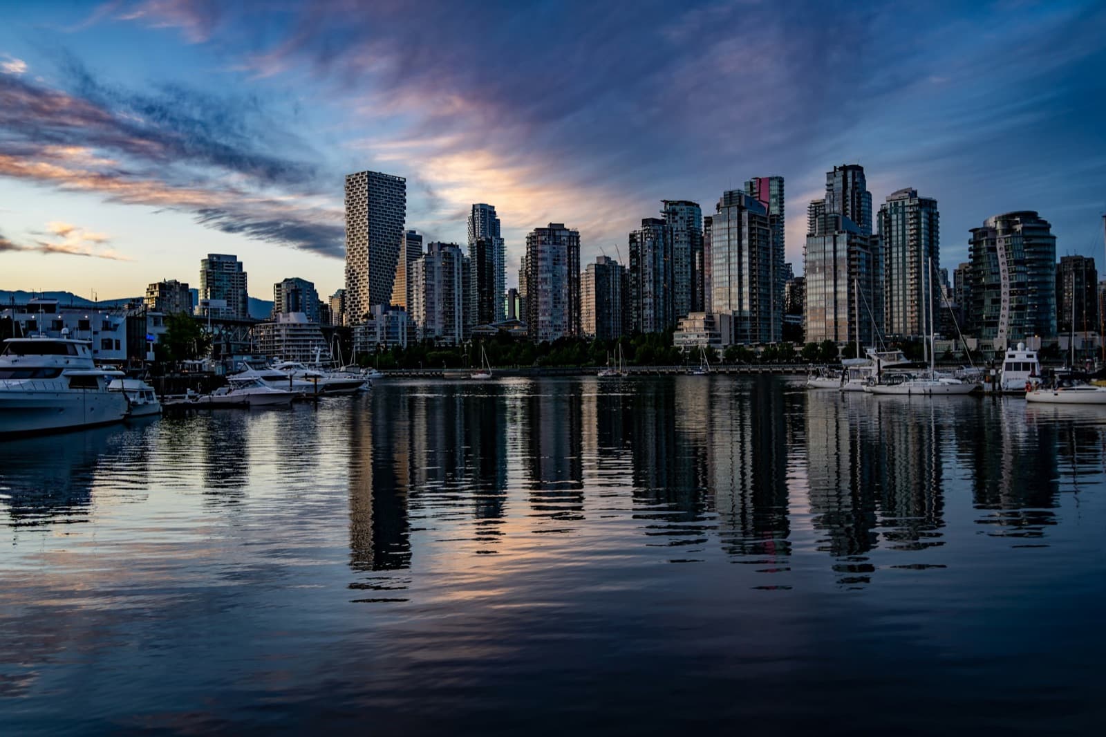 Boats moored below downtown towers under a dusk sky