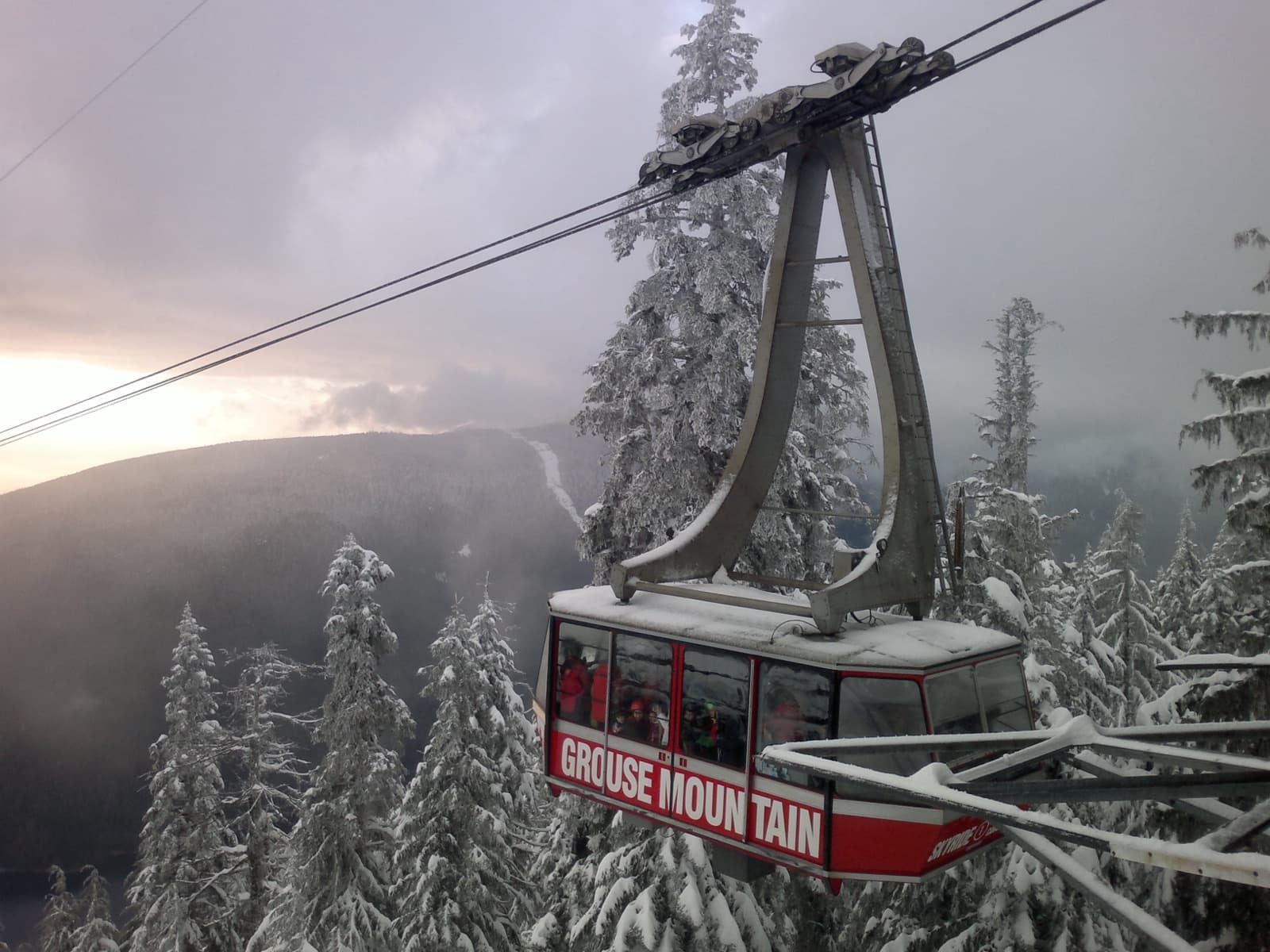 The Grouse Mountain Skyride above snow-covered trees at sunset