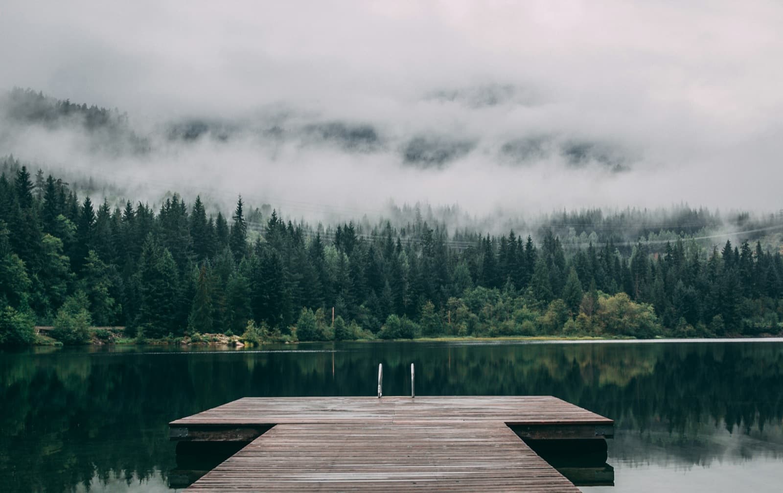 A dock on a still lake below misty forest near Whistler